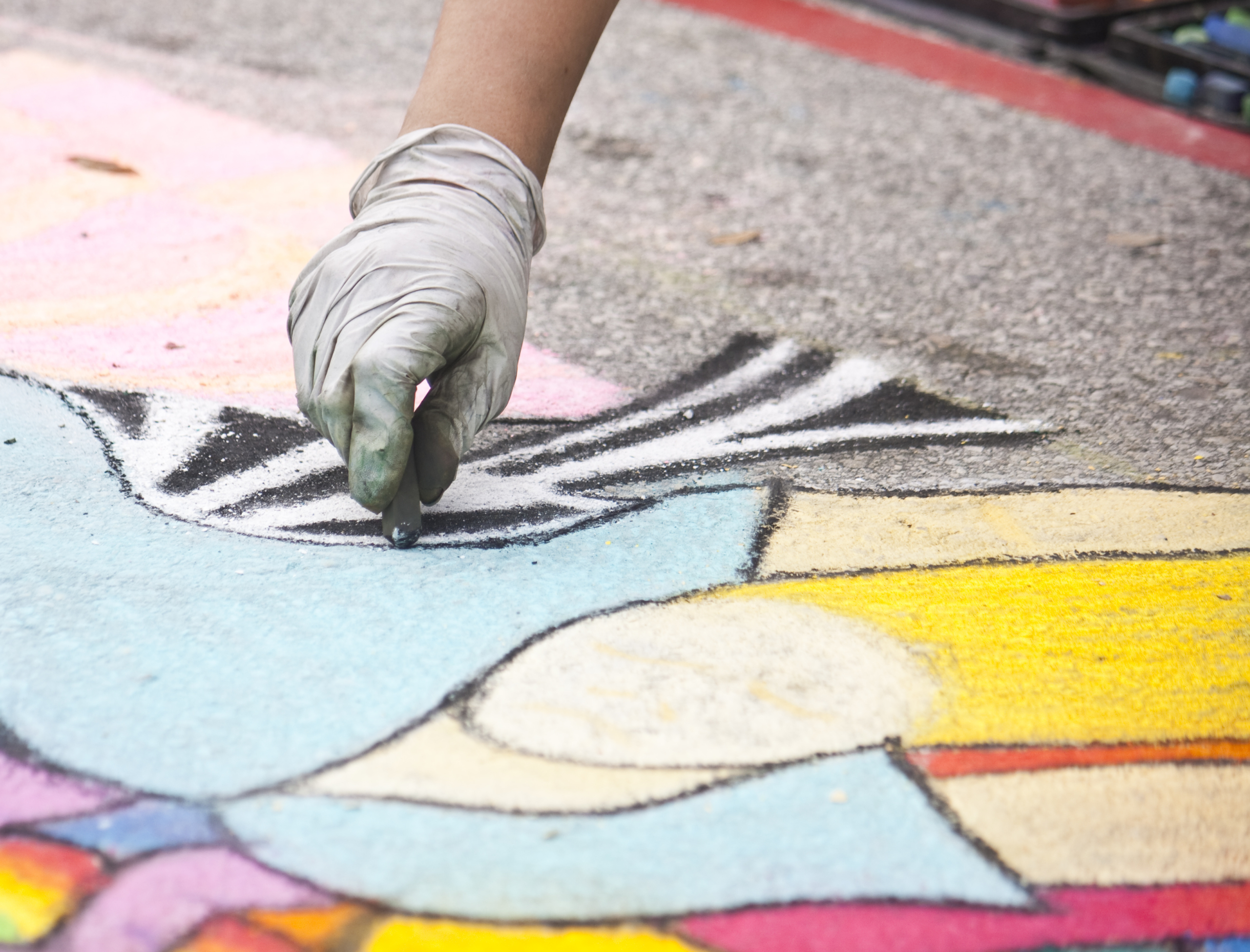 Gloved hand drawing chalk are on asphalt.